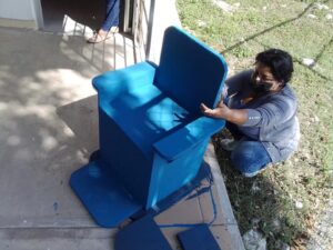 Una maestra termina de pintar de azul el respaldo de una silla pintada de azul