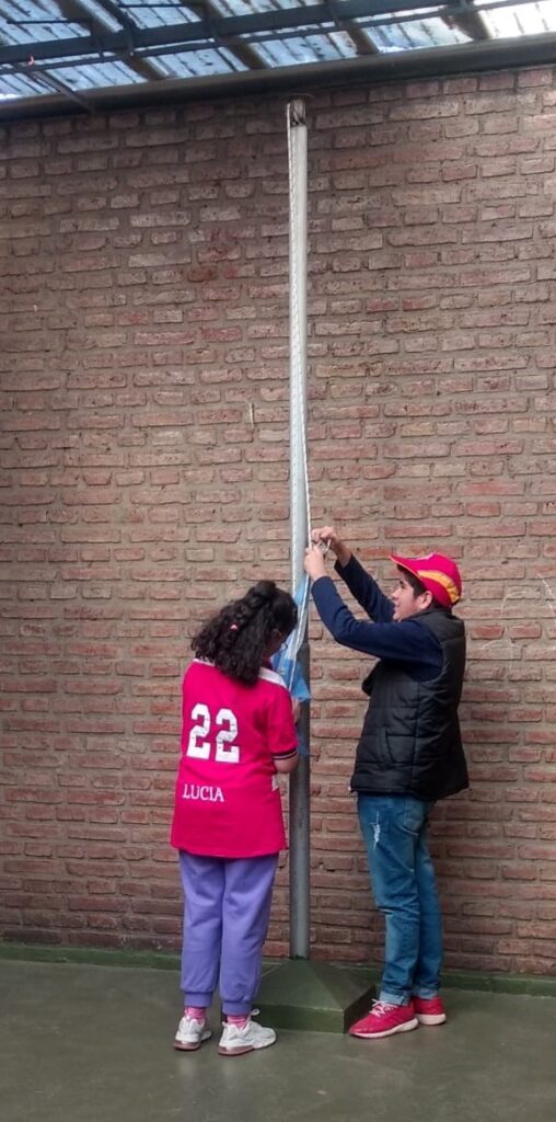 Lucia con su remera de Egreso 2022 izando la bandera con un compañero