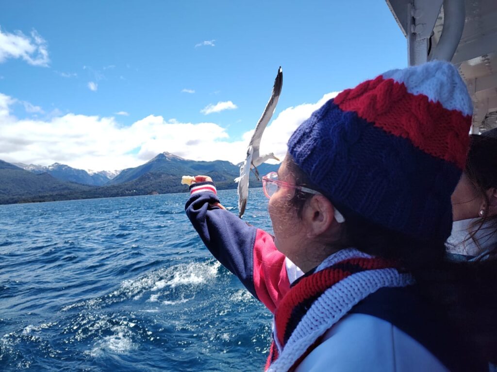 Niño navegando en un catamaran sobre el Lago Nahuel Huapi  y alimentando una gaviota con sus manos.