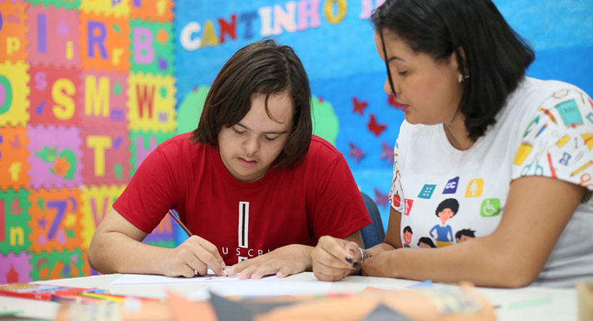 Foto de um aluno e um professor em uma sala de aula colorida trabalhando juntos em uma atividade.