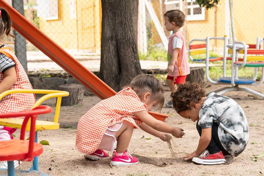 Imagen de dos niños jugando en la arena, fuera de la escuela en un patio de recreo.