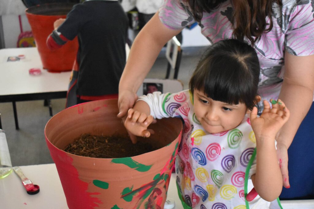 Maestra ayuda a una niña usar una sus manos sobre una maceta.