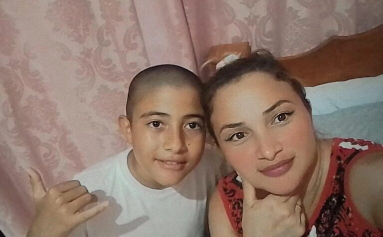 AFoto de rosto de Arthur de 12 anos, com camiseta branca e um leve sorriso, ao lado de sua mãe Elza.