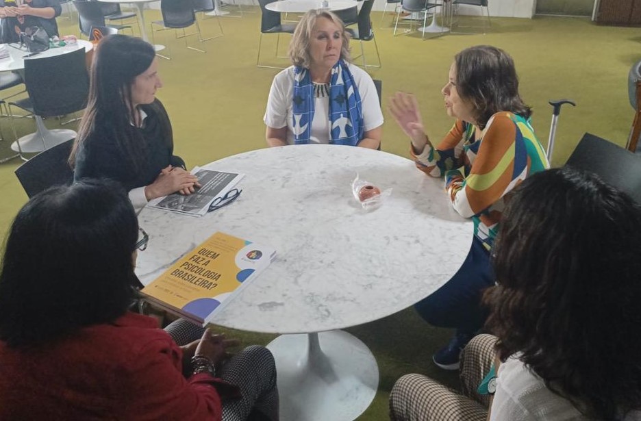 A deputada Erika Kokay e e quatro mulheres do time da Perkins sentadas em volta de uma mesa e conversando.