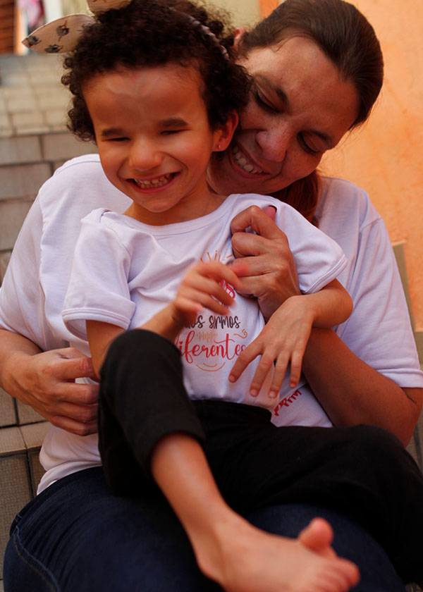 Lidiane e sua filha Micaella sentada em seu colo. As duas usam camiseta branca e sorriem