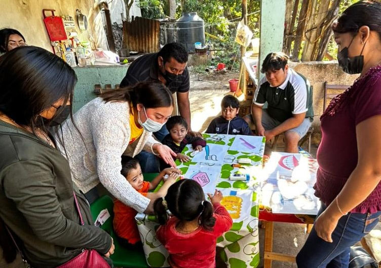 Grupo de familias, maestros y niños reunidos alrededor de una mesa realizando actividades con pictogramas