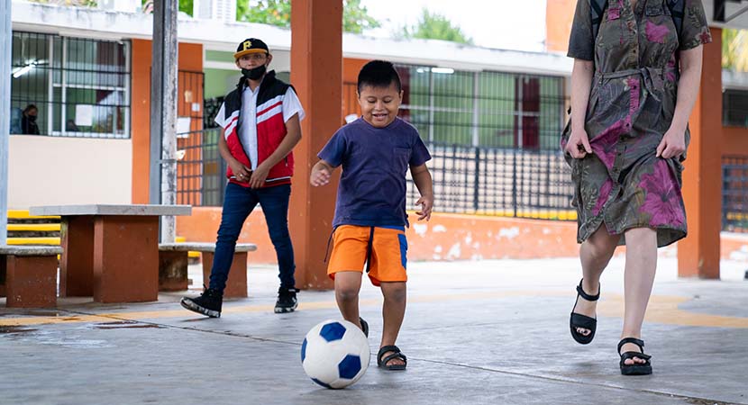 Un niño de primaria juega al fútbol con una maestra. 
