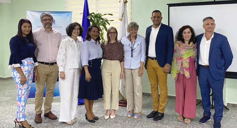 Un grupo de nueve personas entre hombres y mujeres en una sala de reunión, de pie, al lado del otro y posando para una foto grupal oficial.

