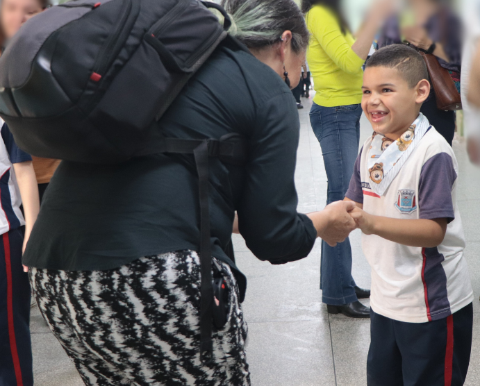 Una foto de Andrea, vista de espaldas. Ella está arrodillada para estar a la altura del alumno Bernardo, quien viste un uniforme escolar azul y blanco. Bernardo sostiene la mano de Andrea y sonríe