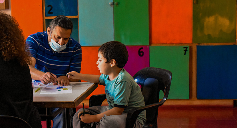 Un maestro y niño sentados en usa mesa trabajando juntos