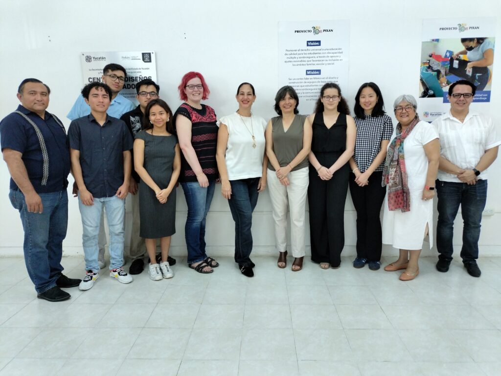 Un grupo de 12 estudiantes y adultos posan frente a una pared blanca. Entre ellos se encuentran estudiantes de MIT D-LAB y Uady, así como personal de Perkins y SEGEY.