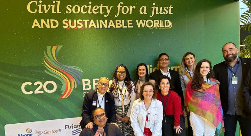 Un grupo de 9 adultos, entre hombres y mujeres, de pie uno junto al otro frente a un panel verde que dice "Sociedad Civil por un Mundo Justo y Sostenible" y presenta un logo de C20.