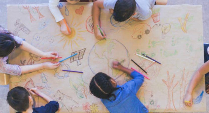 Un grupo de 6 niños dibujan juntos para crear un dibujo grande sobre sustentabilidad en el medio ambiente.