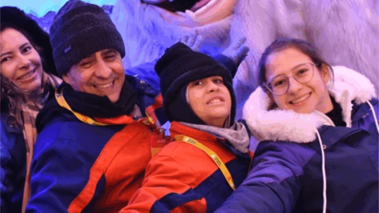 Pedro, os seus pais e a sua irmã, todos vestidos com casacos e chapéus de inverno, sorriem e posam juntos em frente a uma grande estátua de uma criatura de neve, sugerindo um passeio divertido num ambiente nevado ou temático.