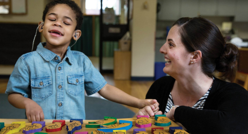 Un niño pequeño trabajando con bloques de señas en una mesa junto a su maestra.