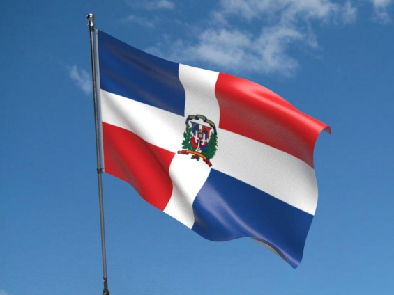 Tras un cielo azul, se ve la bandera de la República Dominicana en azul, rojo y blanco.