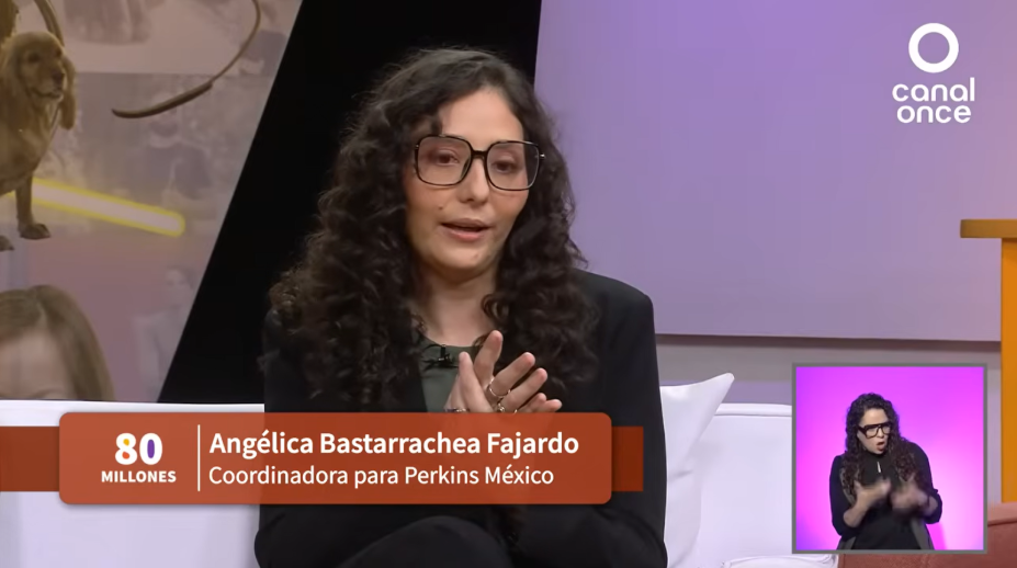 Una mujer con pelo largo y rizado y gafas habla en un programa de televisión. El texto en pantalla dice "Angélica Bastarrachea Fajardo, Coordinadora para Perkins México". Un intérprete de lengua de señas aparece en un pequeño recuadro.