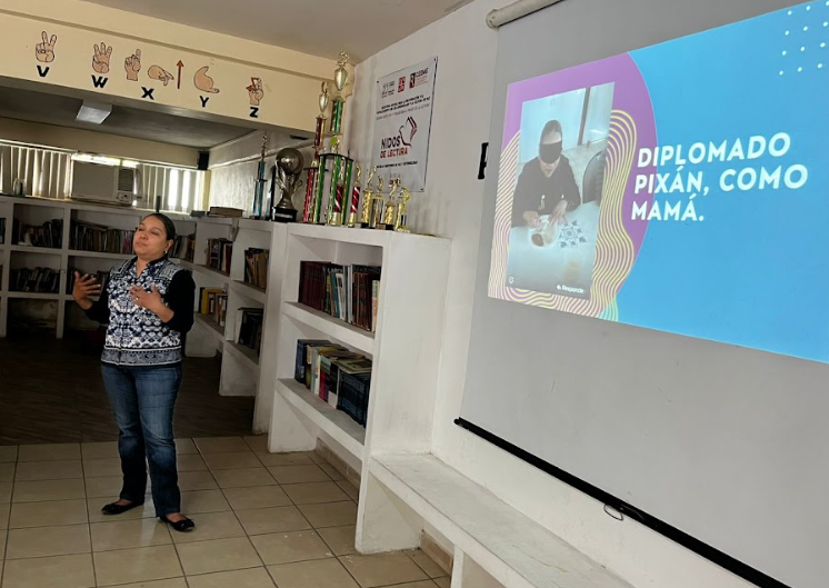 Mujer de pie realiza una presentación. A su lado se proyecta una diapositiva que dice “Diplomado Pixán, como mamá”.