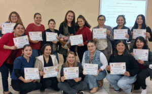 Un grupo de mujeres sostienen certificados, celebrando cierre de capacitación