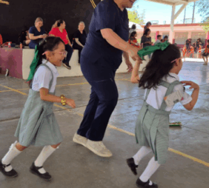Dos niñas con uniforme escolar corren sonrientes en un patio escolar.