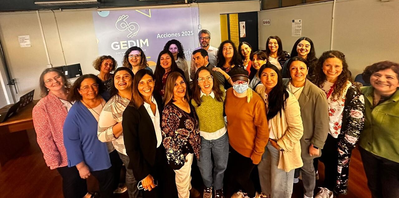 Un grupo de unas 20 personas sonríen y posan juntas en el interior frente a una pantalla que muestra "GEDIM Acciones 2025". El escenario parece ser una oficina o sala de reuniones.