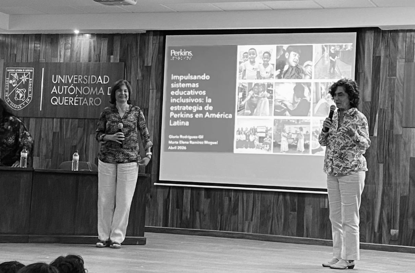 Gloria y Marta Elena están de pie en un escenario, hablando frente a una gran pantalla en la que se proyecta una presentación sobre los sistemas educativos inclusivos en América Latina, en la Universidad Autónoma de Querétaro.