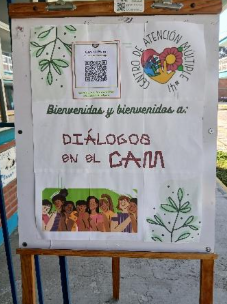 En un tablón de anuncios se ve un cartel de bienvenida a «Diálogos en el CAM» en un Centro de Atención Múltiple, con dibujos de plantas y un grupo de personas sonrientes en la parte inferior.